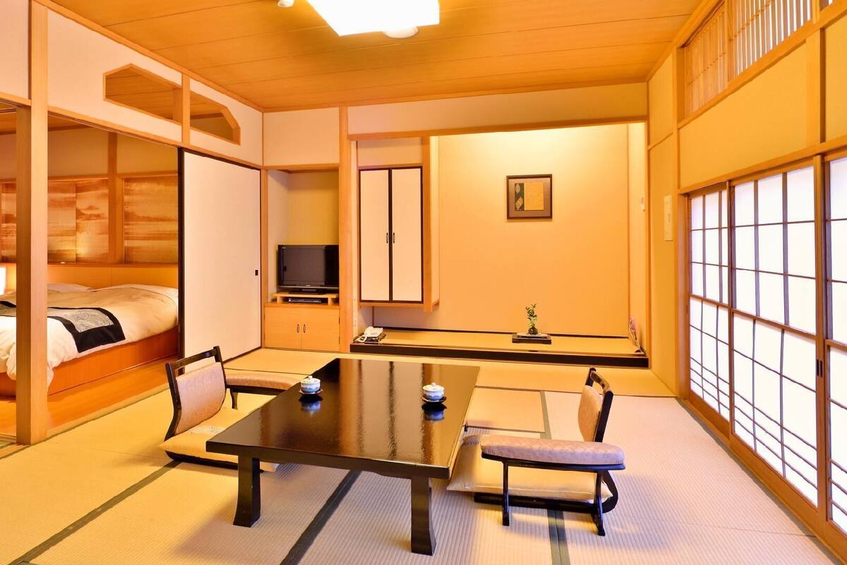 Ein traditioneller japanischer Raum mit Tatami-Boden, einem niedrigen Tisch, einem Bett und Schiebetüren.