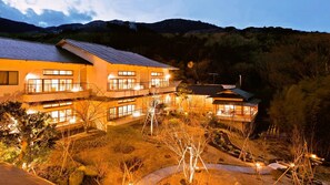 Un hotel de varios pisos con balcones, una fachada bien iluminada y vistas a colinas circundantes.