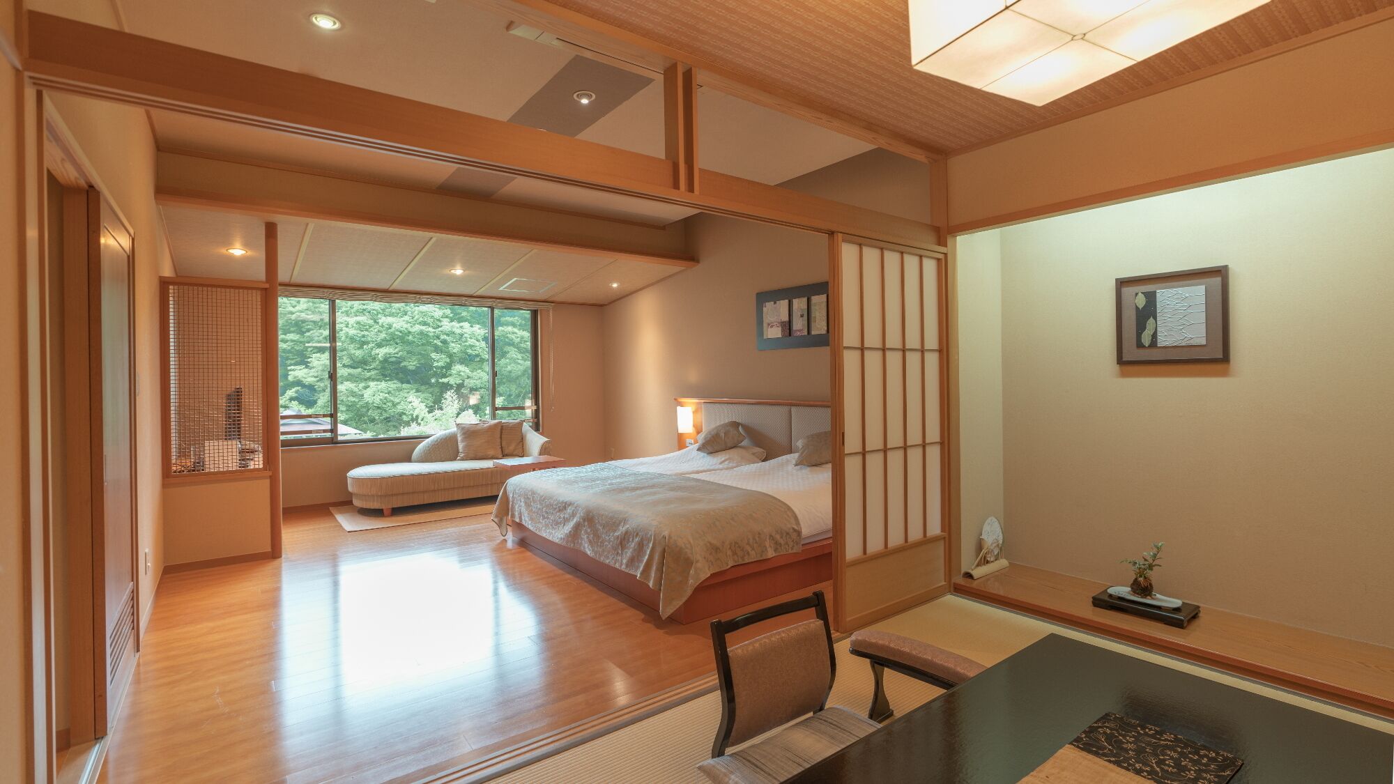 A spacious bedroom with a large bed, a sitting area, and a view of greenery outside.