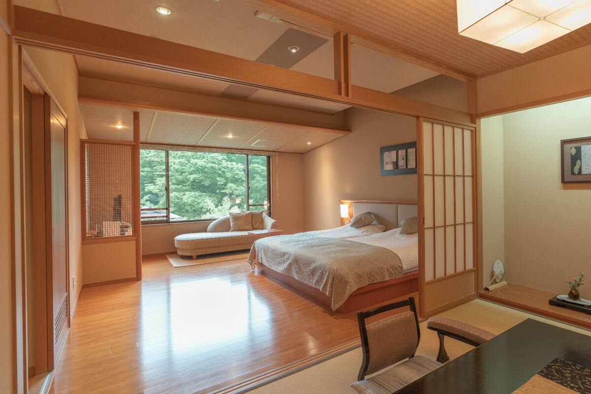 Ein geräumiges Schlafzimmer mit einem großen Bett, einer Sitzecke und Blick auf Grünflächen.