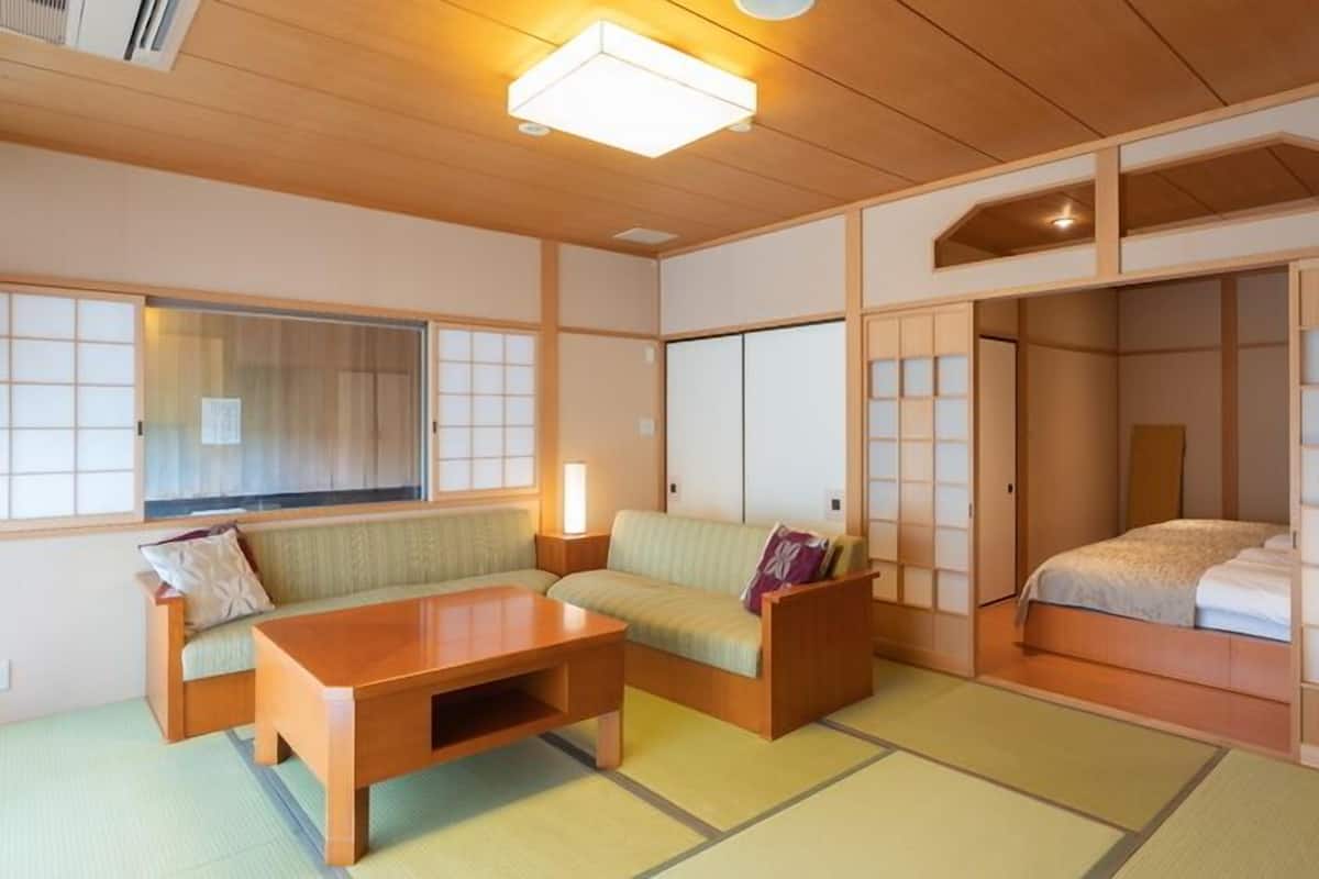 Ein traditioneller japanischer Raum mit Tatami-Böden, einem niedrigen Holztisch, einer Couch und verschiebbaren Shoji-Schiebetüren.