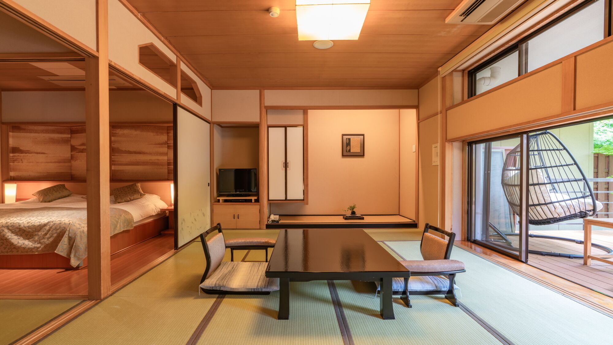 A traditional Japanese-style room with tatami flooring, a low table with cushions, a television, sliding doors, and a view of the outdoors.
