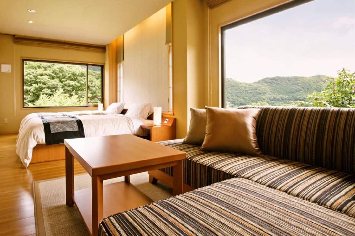 Ein Hotelzimmer mit Bett, einer Sitzecke, einem Tisch und einem großen Fenster mit Blick auf Grünflächen.