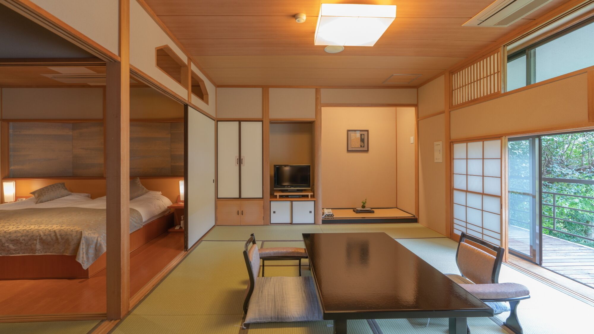 A traditional Japanese-style room with tatami flooring, a low table with chairs, a bed with a headboard, and sliding doors.