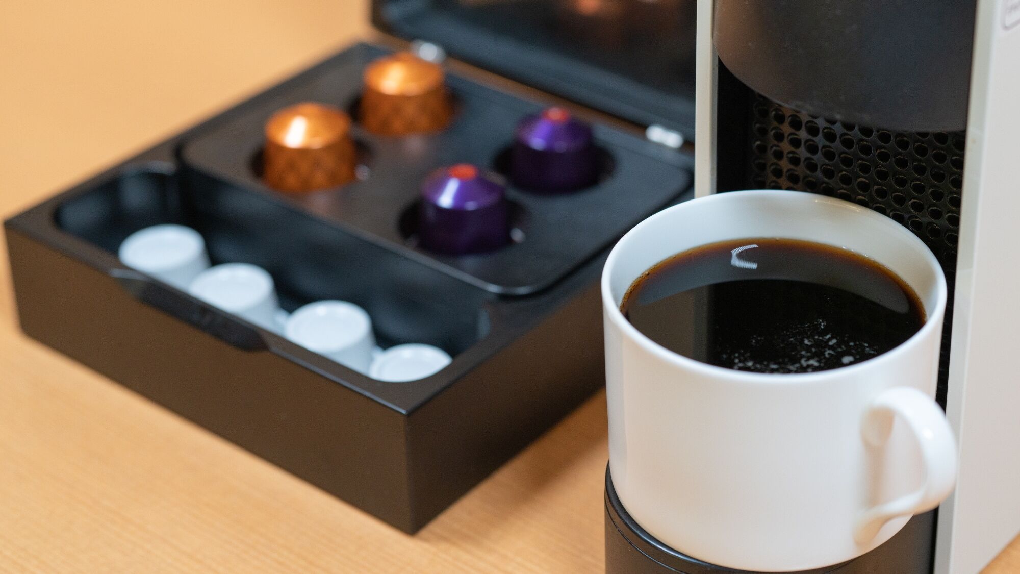 A coffee machine with a cup of coffee and a box of capsules.
