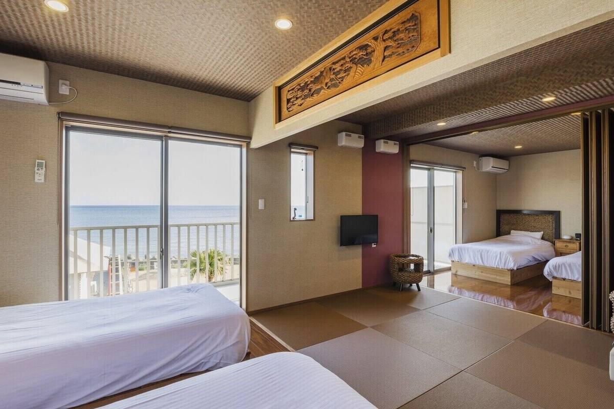 A hotel room with two beds, a TV, and a large window with a view of the sea.