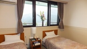 Ein Hotelzimmer mit zwei Betten, einem Nachttisch mit Lampe, einem Telefon und einem kleinen Tisch mit Blumen.