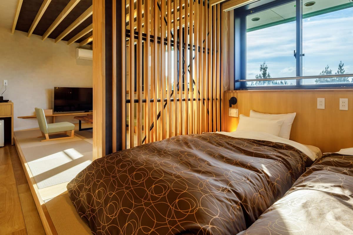 A modern hotel room with a bed, a desk, a chair, a TV, and a window with a view.