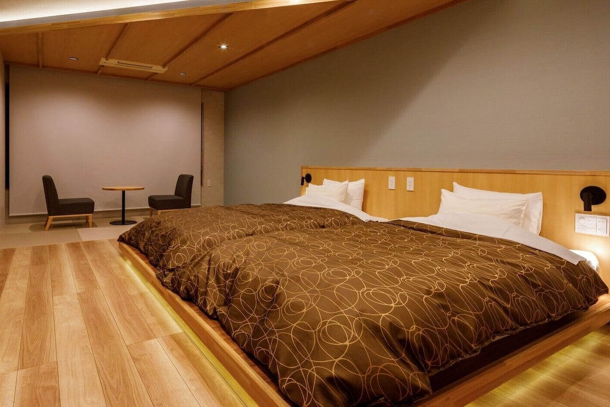 A hotel room with a large bed, a desk with a chair, a small table, and a sofa.