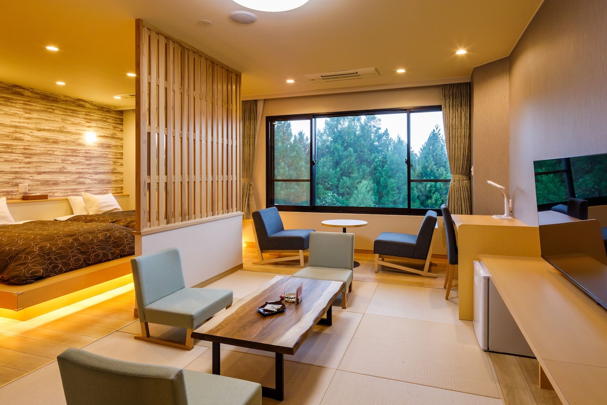 Una habitación de hotel moderna con cama, zona de estar, mesa de comedor y televisor.