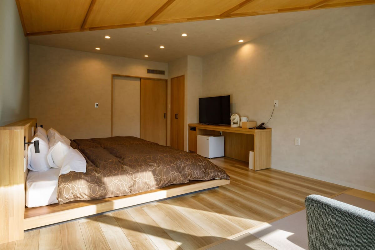 A modern bedroom with a bed, a desk, a TV, and a small refrigerator.