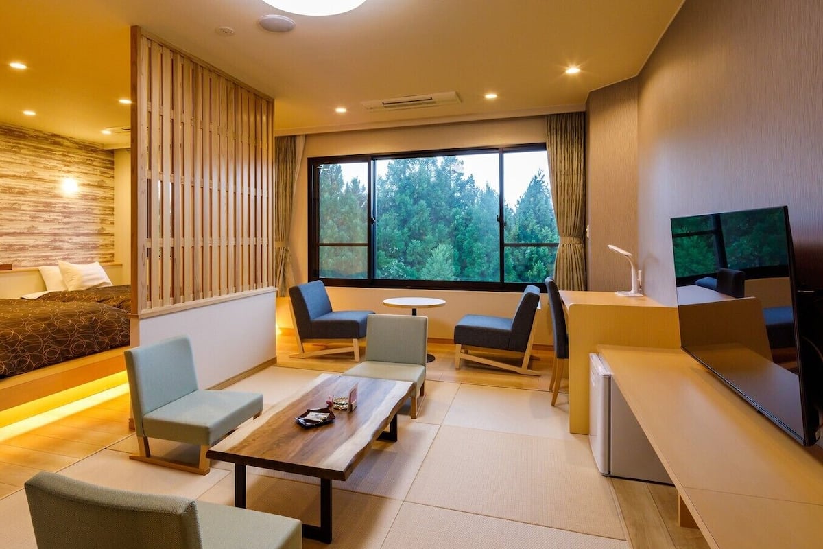 A modern hotel room with a bed, seating area, and a TV.