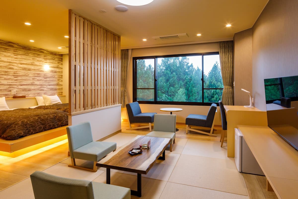 A modern hotel room with a bed, seating area, dining table, and a TV.