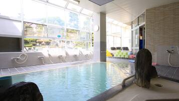 A swimming pool with a view of the outdoors, a shower area, and a seating area with chairs.
