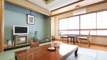 Una habitación japonesa tradicional con suelo de tatami, una mesa baja, un televisor y un ventanal grande.