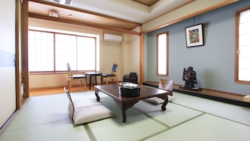 Una habitación tradicional japonesa con suelo de tatami, una mesa baja, sillas y una estatua.
