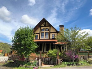 Una casa de dos pisos con techo inclinado, una chimenea y un porche delantero.