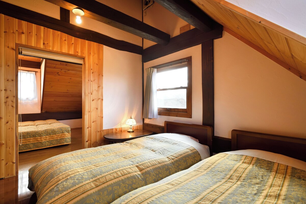 A room with two beds, wooden walls, a window, and a ceiling light.