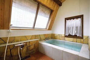 Un baño con bañera, una ventana con cortina y una pared de piedra.
