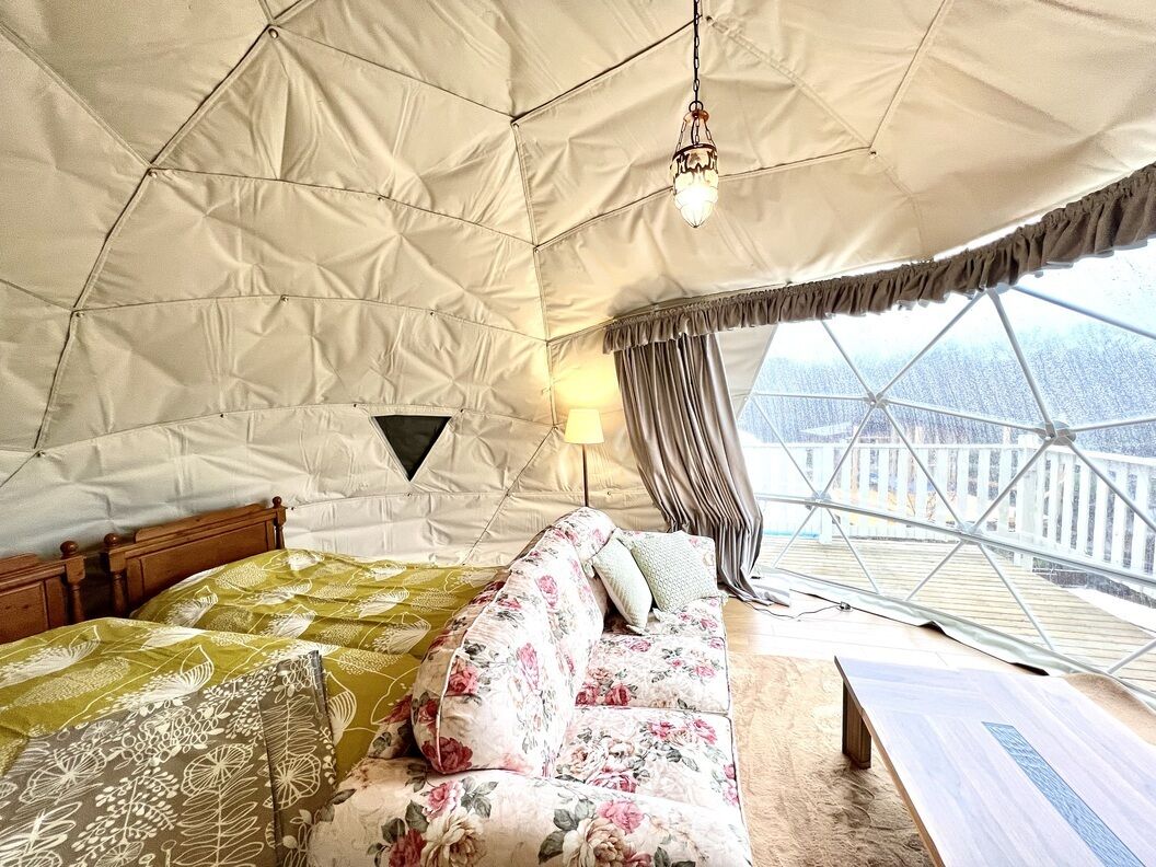 Una habitación con carpa que incluye una cama, un sofá, una lámpara y vistas a través de un gran ventanal.