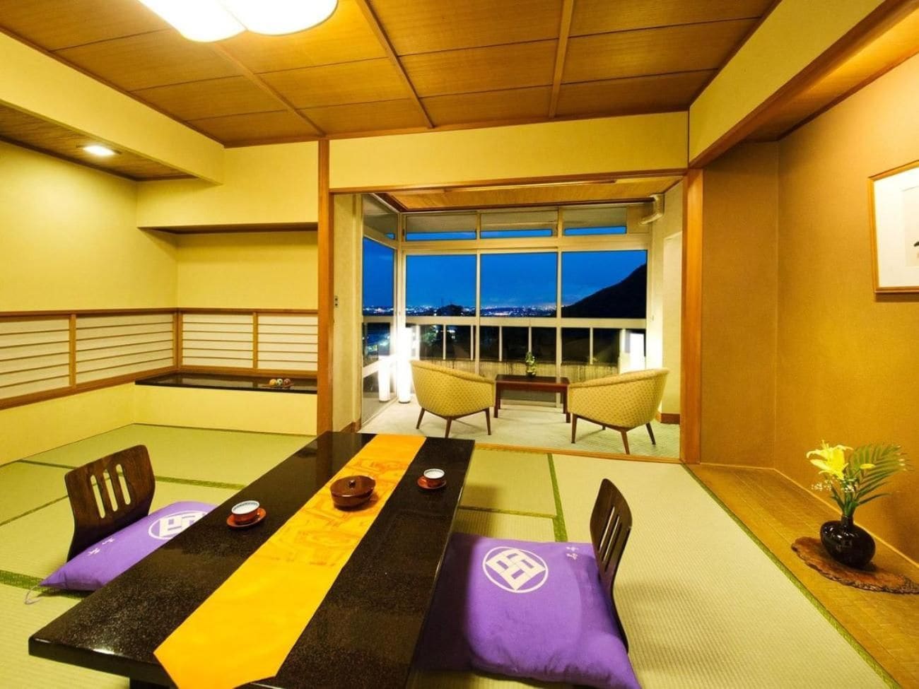 A tatami mat room with a low table, chairs, and a view through a glass door.