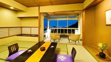 A tatami mat room with a low table, chairs, and a view through a glass door.