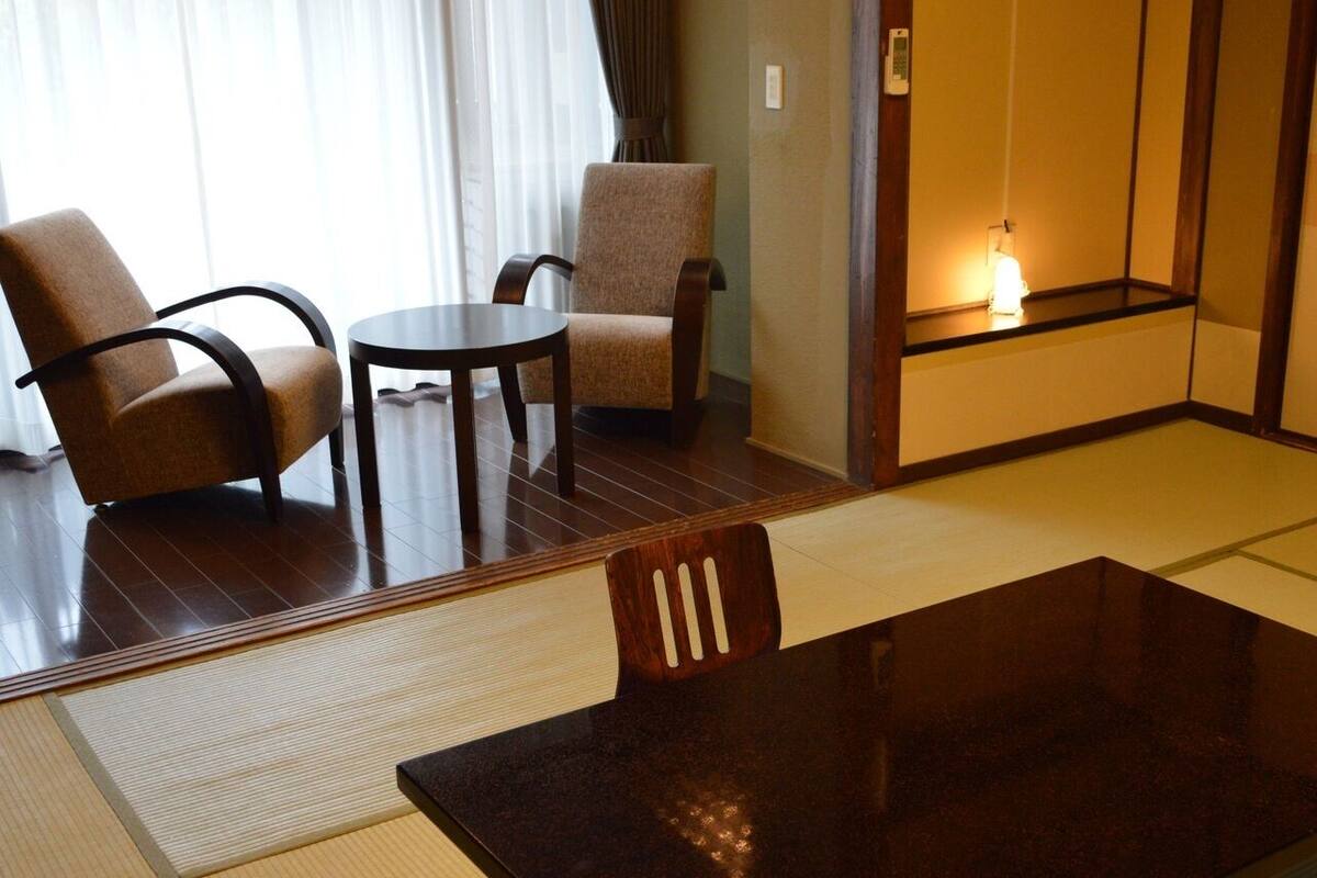 A traditional Japanese-style room with tatami flooring, a low table, two chairs, and a sliding door.