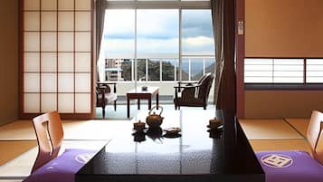 A traditional Japanese room with tatami flooring, a low table with tea set, and sliding doors leading to a balcony with a view.