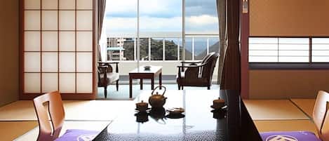 A traditional Japanese room with tatami flooring, a low table with tea set, and sliding doors leading to a balcony with a view.
