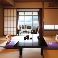 A traditional Japanese room with tatami flooring, a low table with tea set, and sliding doors leading to a balcony with a view.
