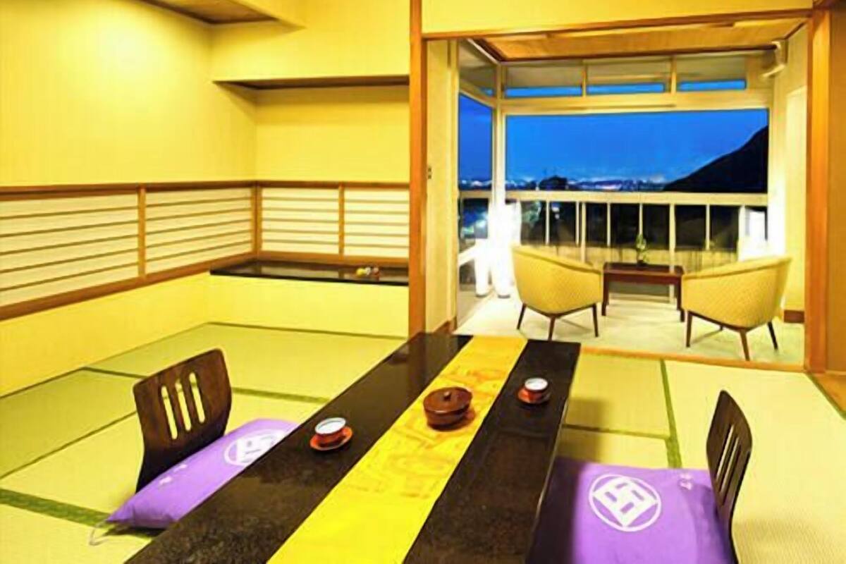 A dining area with a table set for two, a view of the outside, and a balcony with a railing.