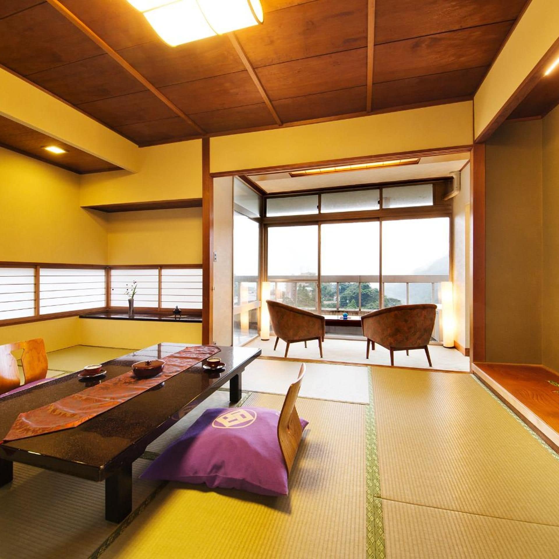 A tatami mat room with a low table, cushions, and a view through large windows.