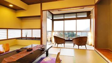 A tatami mat room with a low table, cushions, and a view through large windows.