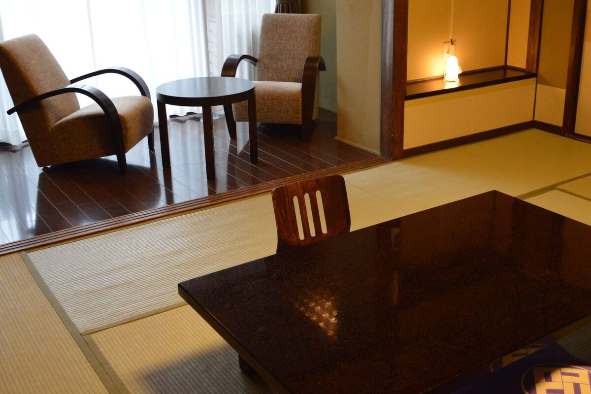 A traditional Japanese room with tatami flooring, a low table, two chairs, and a sliding door.