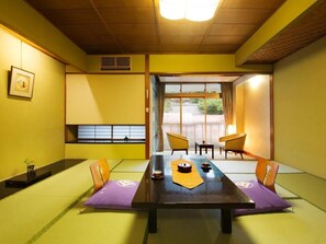 A traditional Japanese room with tatami flooring, a low table with a tea set, and sliding doors leading to an outdoor area.