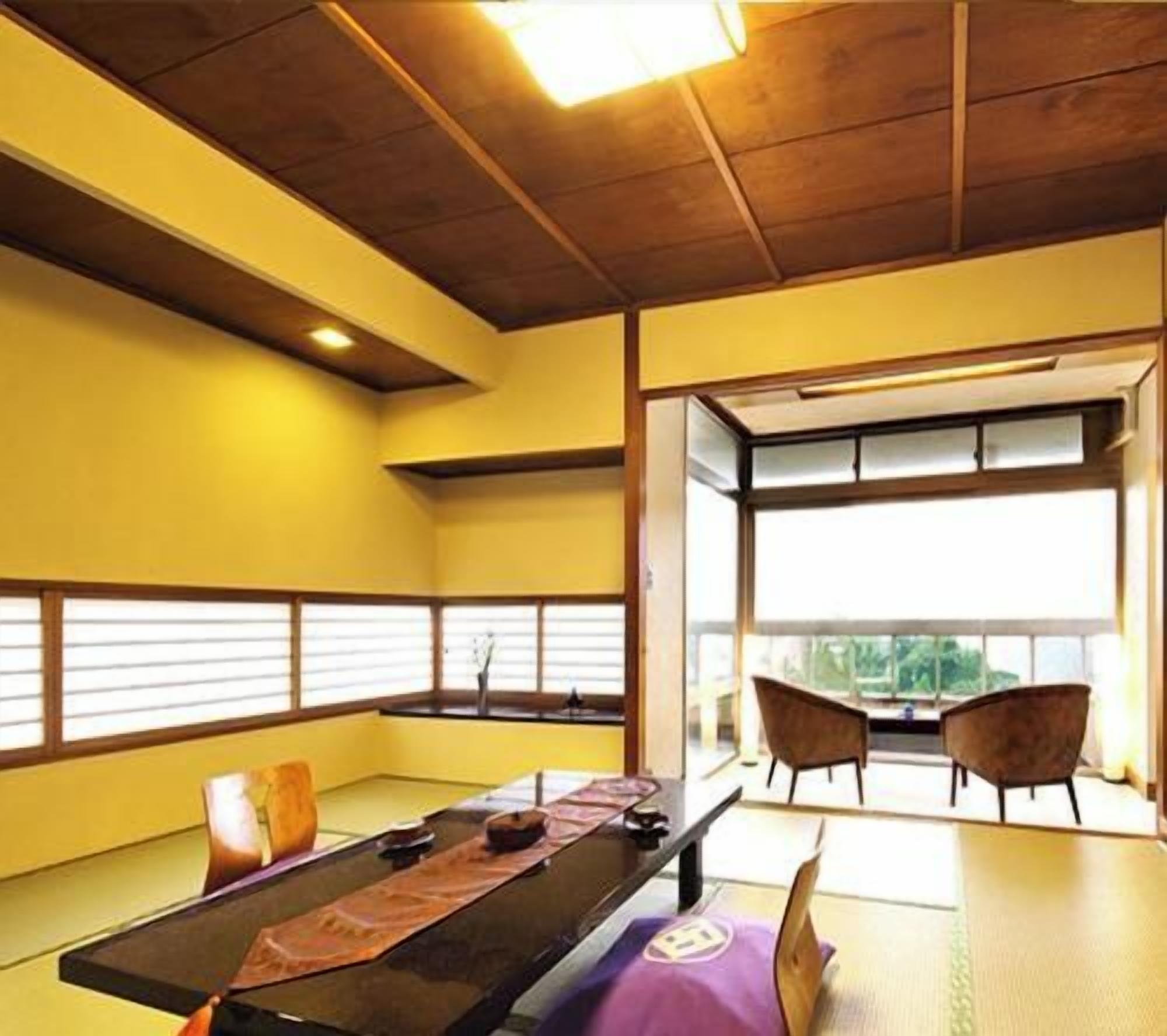 A tatami mat room with a low table, chairs, and a view through a window.