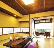 Un espacio con esteras de tatami, una mesa baja, sillas y vistas por una ventana.