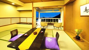A traditional Japanese room with tatami flooring, a low table, cushions, and a view of the city at night. - Kotobukitei (Komono)