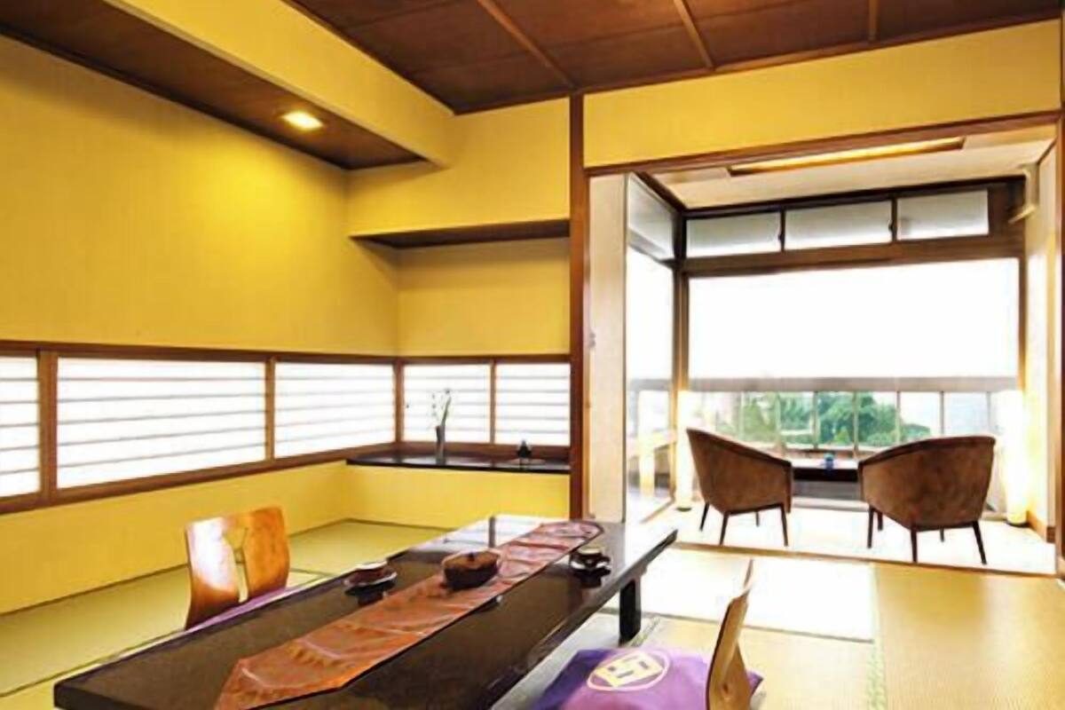 A room with a wooden ceiling, a long table with chairs, and a view through a large window.