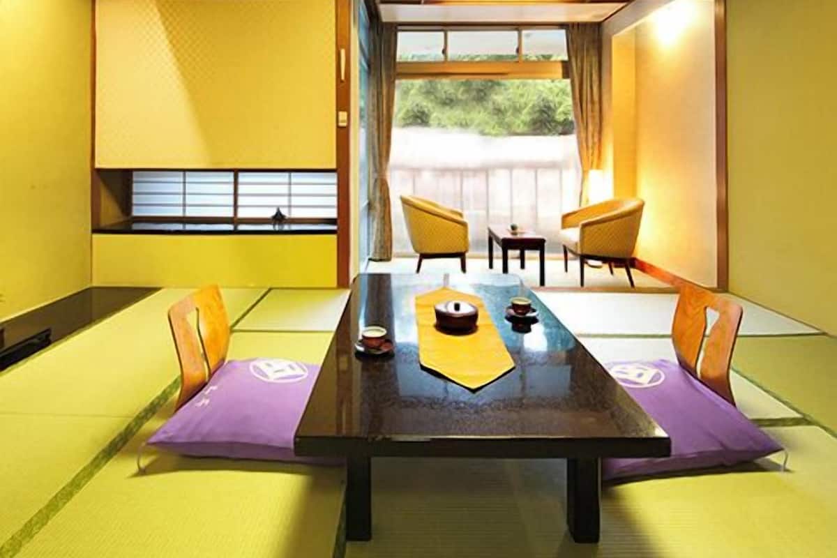 A traditional Japanese-style room with tatami flooring, a low table, and sliding doors leading to an outdoor area.