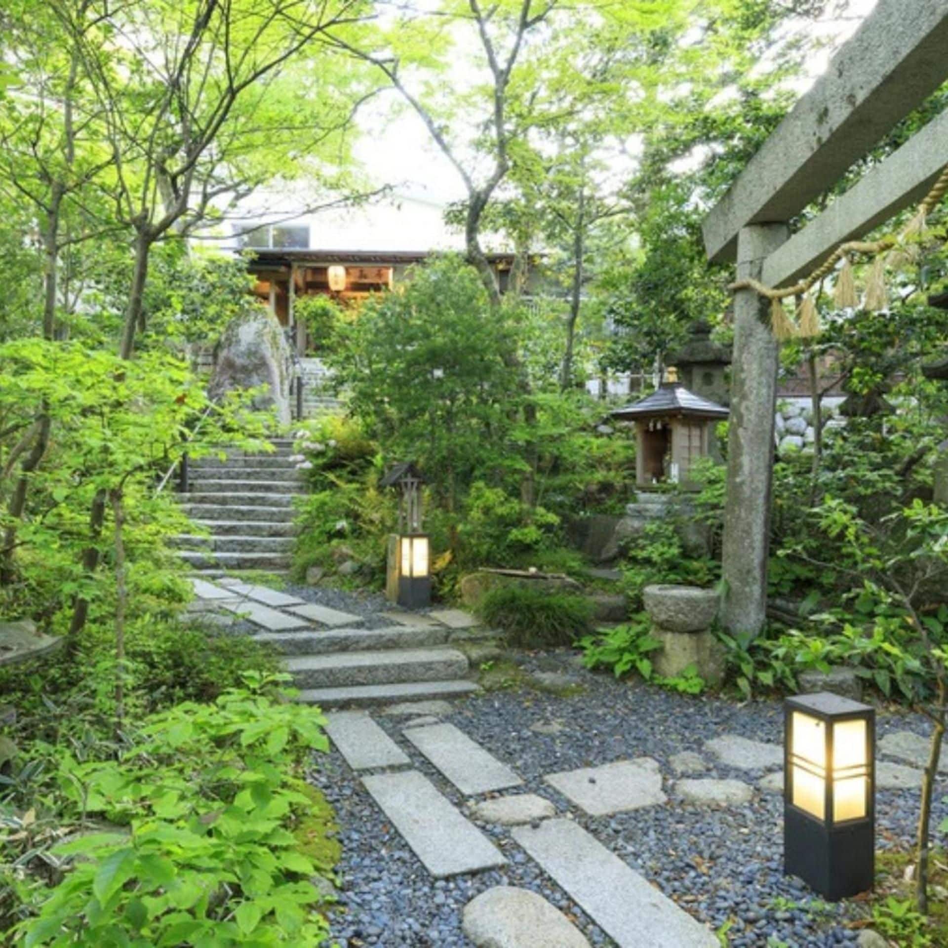 A traditional Japanese garden with stone pathways, lanterns, and a wooden structure.