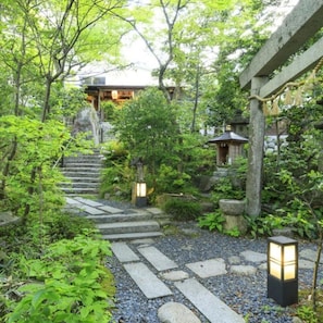 A traditional Japanese garden with stone pathways, lanterns, and a wooden structure.