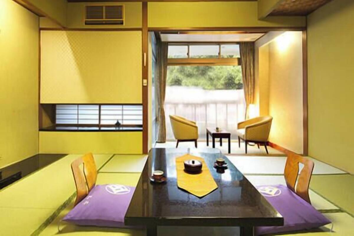 A traditional Japanese room with tatami flooring, a low table, and sliding doors leading to an outdoor area.