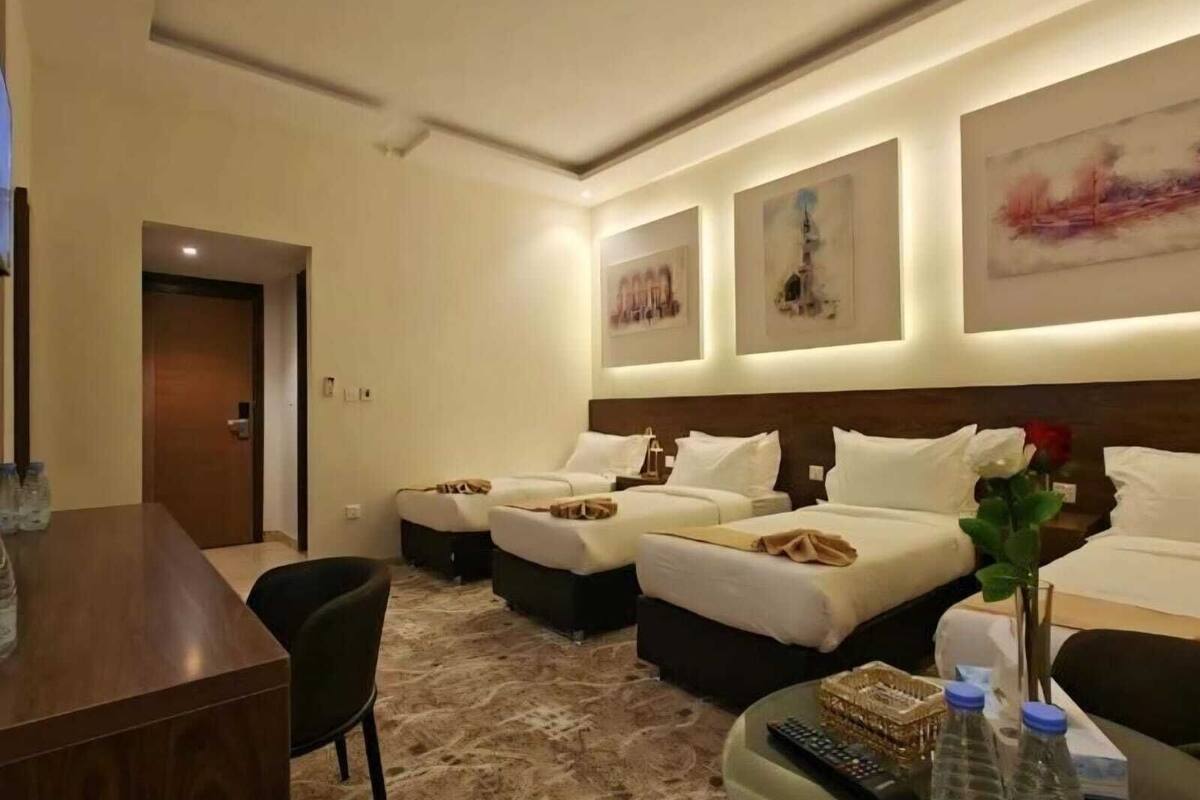 A hotel room with two beds, a desk, a chair, a small table with a remote control, and a vase with a flower.