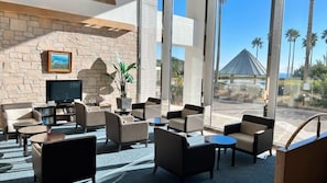 A hotel lobby with stone walls, a television, comfortable seating, and large windows with a view of palm trees and a building. - Hotel Harvest Katsuura (Katsuura)