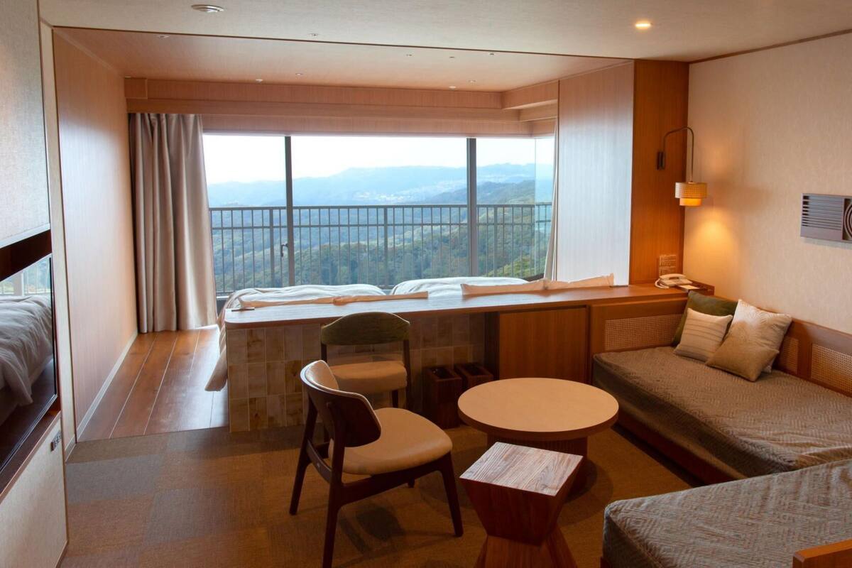 Ein Hotelzimmer mit Bett, Sofa, Schreibtisch, Stuhl, einem kleinen Tisch, einem Fenster mit Blick und einem Wandtelefon.
