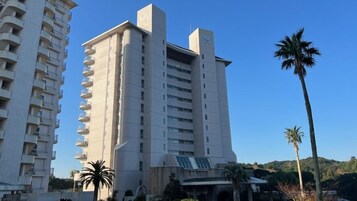 A high-rise building with balconies, a central entrance, and palm trees in the foreground.
