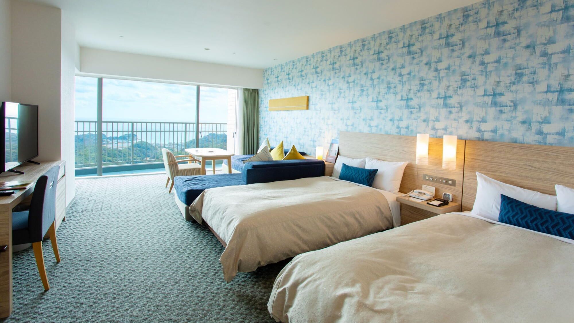 A hotel room with two beds, a desk, a chair, a TV, and a balcony with a view.