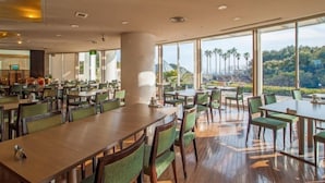 A spacious dining area with high ceilings and large windows offering a view of palm trees and hills. - Hotel Harvest Katsuura (Katsuura)
