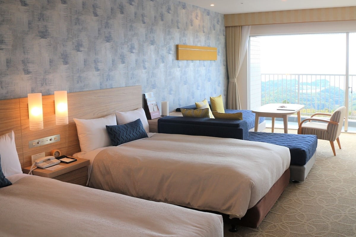 Ein Hotelzimmer mit zwei Betten, einem kleinen Tisch, einem Stuhl und einem Balkon mit Blick.